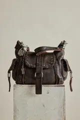 Cartera mini de cuero marrón con terminación gastada, cuerpo blando, bolsillos exteriores y solapa con cierre de hebilla. Incluye herrajes metálicos envejecidos y detalles colgantes con candado y llave.