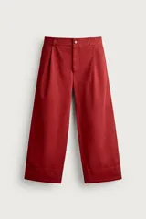 Pantalón wide fit color rojo terracota, con pliegues frontales, bolsillos laterales y cierre frontal con cremallera y botón.