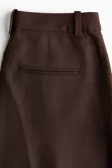 Pantalón sastrero de tiro alto color marrón, de corte recto y amplio, confeccionado en mezcla de lino y viscosa. Cuenta con trabillas para cinturón, cierre frontal oculto con botón y bolsillos laterales.