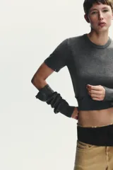 Jersey de punto gris oscuro, cuello redondo y manga larga. Presenta detalles desmontables con botones a lo largo de las costuras de las mangas y en el ruedo inferior.