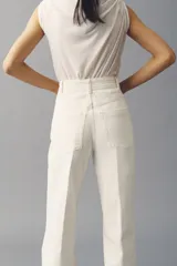 Jean de denim de algodón color blanco, de tiro alto y piernas amplias con corte holgado. Cuenta con pliegues frontales y traseros, cierre frontal con botón y bolsillos traseros de parche.