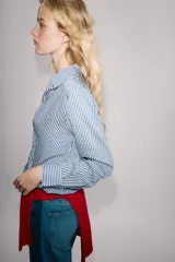 Camisa de cuello solapa y manga larga, con bajo ajustable mediante cordones y cierre frontal con botones ocultos. Diseño a rayas blancas y azules.