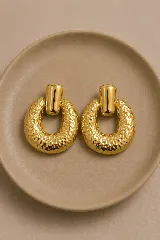 Aros de estilo vintage con diseño de argolla martillada y pieza superior lisa en acabado dorado brillante.