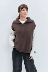 Cardigan de punto con diseño bicolor, cuerpo en color marrón y mangas largas en color crema con textura trenzada. Presenta cuello polo, cierre frontal con cremallera y puños acanalados.