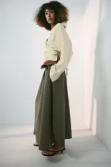 Falda midi tipo capa de tiro medio, confeccionada en mezcla de algodón color verde militar. Cuenta con cintura con trabillas, bolsillos de vivo en los laterales, cierre lateral con cremallera oculta y aplicación de cinturón marrón de estilo western con hebilla metálica grabada.