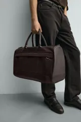 Bolso de viaje marrón con textura grabada, cierre de cremallera, bolsillo interior con cremallera, bolsillo frontal con cremallera, doble asa de mano y asa de hombro ajustable y extraíble.