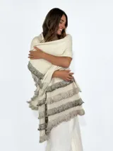 Pashmina color beige con flecos en tonos grises y beige. Tejido de punto calado con detalle de volados. Ideal para usar como chal o bufanda.