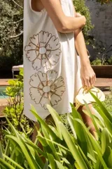 Vestido corto de algodón color blanco, con diseño holgado, cuello redondo y mangas cortas. Presenta detalles de bordados florales en los laterales.