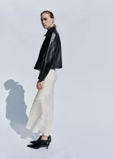 Chaqueta corta de cuero negro con textura efecto cocodrilo, diseño recto, cuello camisero, manga larga, bolsillos laterales de ribete y cierre de doble botonadura.