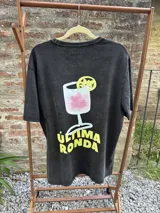 Remera negra con efecto gastado, de corte holgado y manga corta. Estampa en la espalda de una copa con un trago rosado y una rodaja de limón, con la frase "Última Ronda" en amarillo.