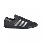 Championes urbanos Adidas modelo Hamburg, confeccionados en gamuza color azul marino con las icónicas tres tiras laterales y detalle en el talón en color plateado. Presenta el nombre del modelo en letras doradas y suela de goma al tono.