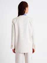 Blazer blanco con finas rayas verticales negras, solapas con muesca, cierre con un botón dorado y bolsillos delanteros con solapa.