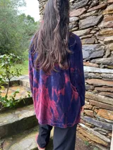 Polerón de plush azul con efecto batik en tonos rojizos, cuello alto holgado, mangas largas raglán, bolsillos frontales tipo parche y aberturas laterales para lactancia con dobladillo trasero más largo.