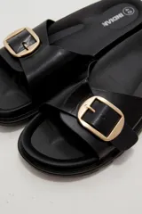 Sandalia plana de eco cuero negro, con tira ancha en el empeine decorada con una hebilla metálica dorada cuadrada y suela dentada.
