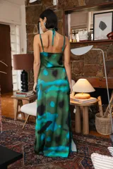 Vestido largo de satén con estampado abstracto en tonos verdes y azules, con escote halter cruzado, detalle de frunce en el pecho y tajo lateral profundo.
