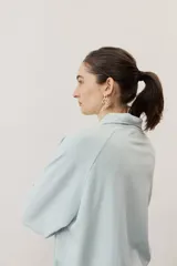 Buzo celeste de manga larga con cuello polo y cierre frontal de botones. Presenta un parche marrón bordado en el pecho.