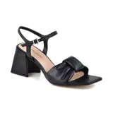 Sandalia de cuero sintético color negro, con taco cuadrado, tira ancha sobre el empeine con detalle de nudo y pulsera al tobillo con hebilla.