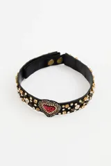 Gargantilla tipo choker de color negro, con apliques de strass y cristales en toda la banda. Presenta un dije central en forma de corazón decorado con piedras rojas y brillantes.