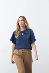 Top negro de manga corta con detalle de nudo en el escote y abertura tipo gota. Presenta una silueta relajada y textura sutil en la tela.