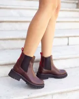 Botas tipo Chelsea de cuero color marrón, con paneles laterales elásticos en negro y tirador trasero en color rojo. Presentan una suela track robusta de goma negra con costuras decorativas en rojo.