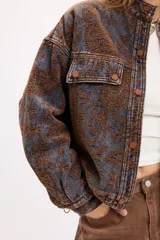 Campera de jean con diseño de estampado paisley en tonos marrones y grises. Presenta un corte relajado, cuello camisero, cierre frontal con botones metálicos y bolsillos frontales con solapa.