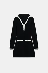 Vestido corto de tejido suave, color negro con detalles en blanco. Presenta cuello solapa, escote en pico, manga larga, falsos bolsillos delanteros y cierre frontal con botones dorados.