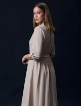 Vestido maxi color beige, con cuello mao y escote en V. Presenta mangas largas con presilla y botón para regular el largo, y un lazo ajustable en la cintura que marca la silueta.