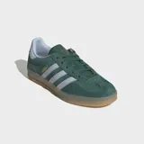 Championes Adidas Gazelle Indoor de gamuza verde oscuro, con las tres tiras características en color blanco y el nombre del modelo en letras doradas en el lateral. Poseen suela de goma translúcida y detalles en color celeste claro en el talón.