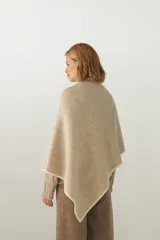 Ruana de tejido de punto industrial en color marrón, confeccionada en lana fina sin teñir. Presenta un diseño con doble ojal que permite mantener la prenda cruzada y cerrada.