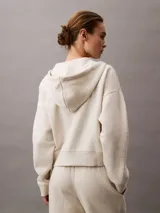 Buzo con capucha y cierre frontal completo, color beige jaspeado, confeccionado en suave fleece de mezcla de algodón y poliéster. Presenta bolsillos laterales y el logo Archive de Calvin Klein bordado en el pecho.