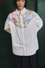 Camisa de corte oversize con mangas largas y puños abotonados. Presenta un diseño bicolor con cuerpo blanco y un canesú delantero con estampado floral multicolor.