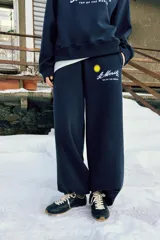 Pantalón de felpa azul marino con tiro alto, cintura elástica con cordón ajustable y diseño de pierna ancha. Presenta un estampado frontal con el logo de St. Moritz y un sol amarillo.
