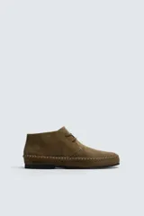 Zapato tipo derby de cordones, confeccionado en piel con acabado de serraje. Presenta costuras decorativas en el contorno de la suela, horma redonda y suela de goma Vibram.