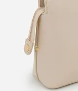 Cartera bandolera pequeña de diseño estructurado en color beige, confeccionada en poliuretano con acabado liso. Presenta un diseño geométrico con costuras en relieve en la parte frontal, cierre superior con cremallera y una elegante correa de cadena metálica en tono dorado.