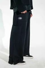 Pantalón de corte holgado y estilo urbano, color negro, con cintura elástica ajustable mediante cordón y bolsillos laterales. Presenta un pequeño estampado en la pierna derecha.