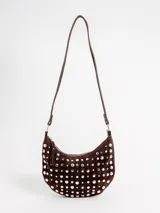 Cartera tipo bandolera de gamuza negra en forma de media luna, completamente decorada con tachas metálicas plateadas de distintos tamaños. Cuenta con un asa ajustable para llevar al hombro o en la mano y cierre superior con cremallera.