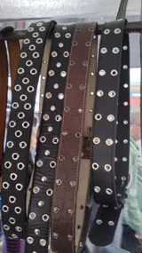 Cinturón negro de cuero con doble hebilla plateada y ojalillos metálicos.