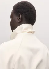 Chaqueta de mezcla de lana, poliéster y elastano color marfil, con solapas cruzadas, cuello alto y cinturón ajustable del mismo tejido. Cuenta con mangas largas y forro interior de viscosa.
