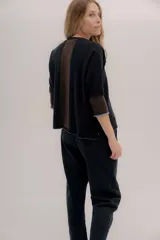 Buzo de punto en color negro con mangas tres cuartos y puños en contraste color marrón. Presenta un diseño holgado con tajos laterales y un aplique circular con logo en la parte inferior.