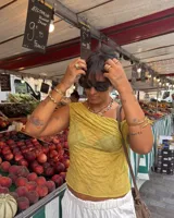 Collar corto de estilo artesanal, compuesto por una variedad de piedras naturales en tonos tierra, verdes, rojos y amarillos, intercaladas con pequeñas perlas de río. Presenta dijes de bronce macizo con formas orgánicas, incluyendo una figura de pez y un dije circular central, unidos por un cierre de barra y argolla.