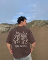 Remera marrón oversize de manga corta con estampado gráfico en la espalda de dos gatos de estilo retro con cuchillos y texto "Kahoa Industries".