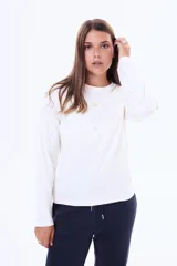 Remera de manga larga en color blanco, con cuello redondo y corte clásico. Presenta una pequeña etiqueta decorativa en el centro del pecho.