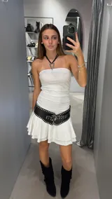 Vestido corto de color blanco con diseño strapless y falda con volados en el ruedo. Presenta un ajuste entallado en el torso con frunces laterales.