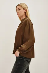Camisa de viscosa en color marrón, con cuello clásico, cierre frontal de botones y mangas largas con puños abotonados.