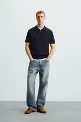 Polo de punto negro, manga corta, con cuello solapa y cierre frontal de tres botones. Presenta un calce regular y acabados en rib en mangas y ruedo.