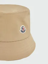 Gorro tipo bucket de algodón color beige, con diseño clásico de ala corta y logo de la marca aplicado en el frente.