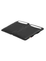 Billetera artesanal de cuero marrón oscuro con costuras en hilo rojo. Presenta un sistema de sujeción elástico en el lateral con detalles de colores (rojo, amarillo, azul) y ranuras para tarjetas en el exterior.