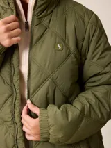 Campera larga acolchada con diseño de rombos, cierre frontal completo y cuello alto. Presenta puños elásticos y un pequeño logo aplicado en el pecho.