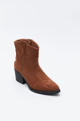 Bota corta estilo western de gamuza color marrón, con taco cuadrado negro y puntera estilizada. Presenta un detalle de estrella aplicada en el lateral y tirador en la parte superior.
