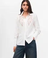 Camisa blanca de manga larga con detalles bordados calados en el frente y puños anchos.